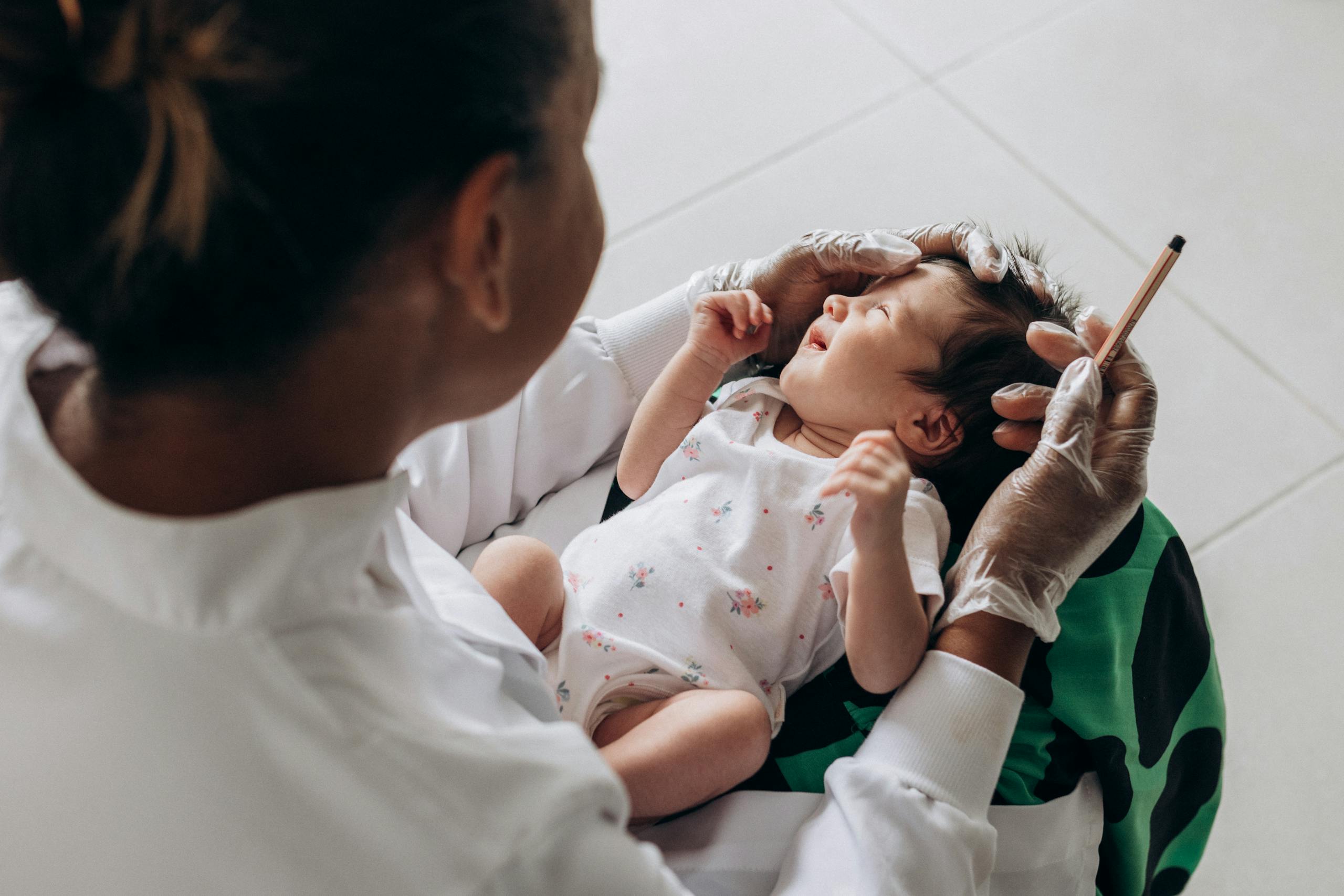 A woman is holding a baby while another person is holding a syringe