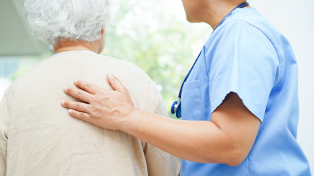 Nurse comforting a care home resident, with their hand the residents back.