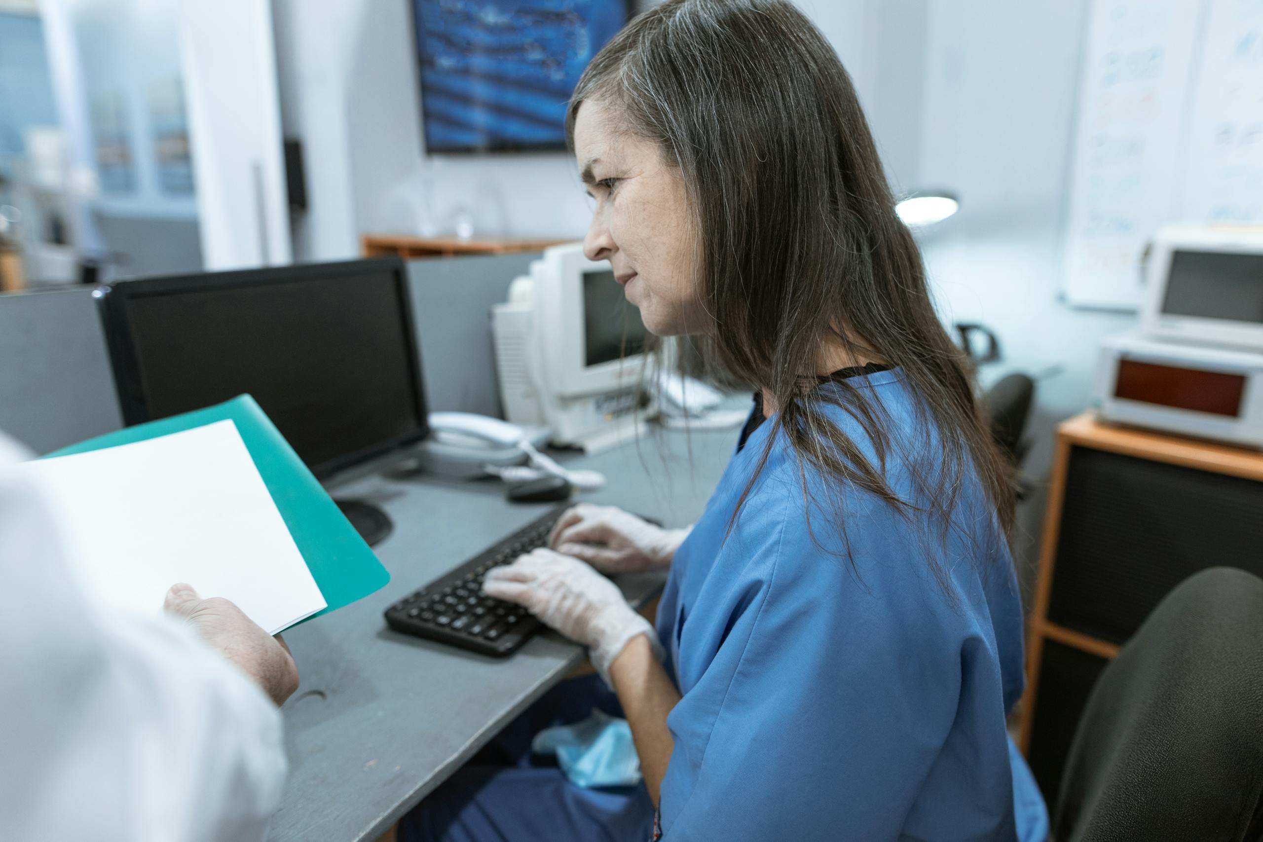 Nurse in scrubs typing on a keyboard at a medical workstation.